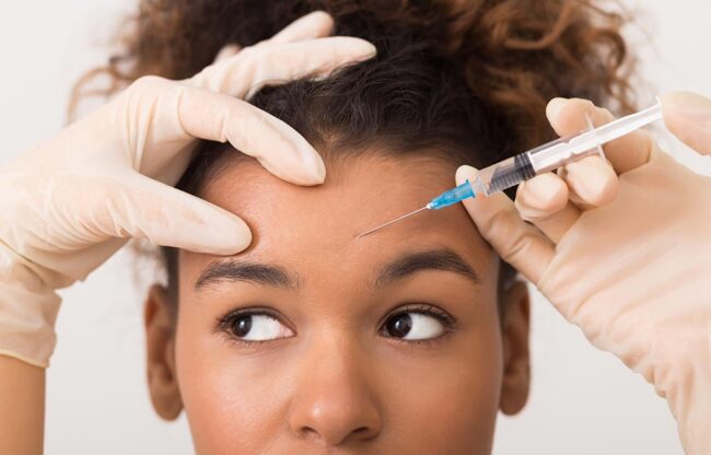 African american woman getting botox injection in forehead African american woman getting botox injection in forehead