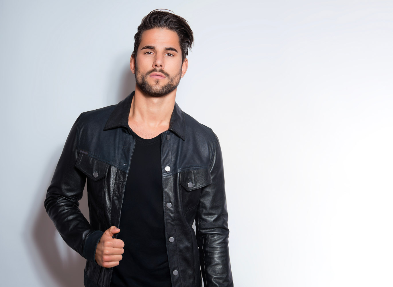 Hair restoration-2 A main in a leather jacket poses in front of a wall